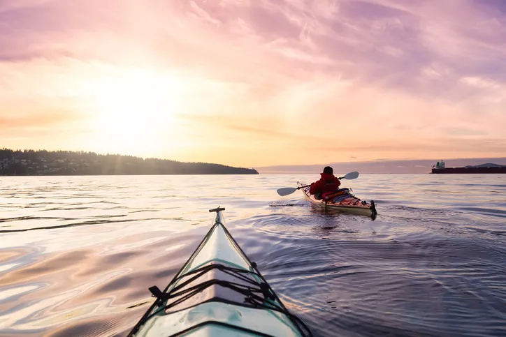 Two kayakers are on a smooth surfaced lake while the sun is setting.